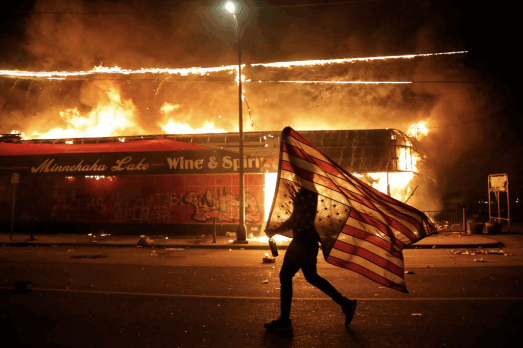 A protester carries a U.S. flag upside down as he walks past a burning building in Minneapolis in 2020. Julio Cortez / AP file